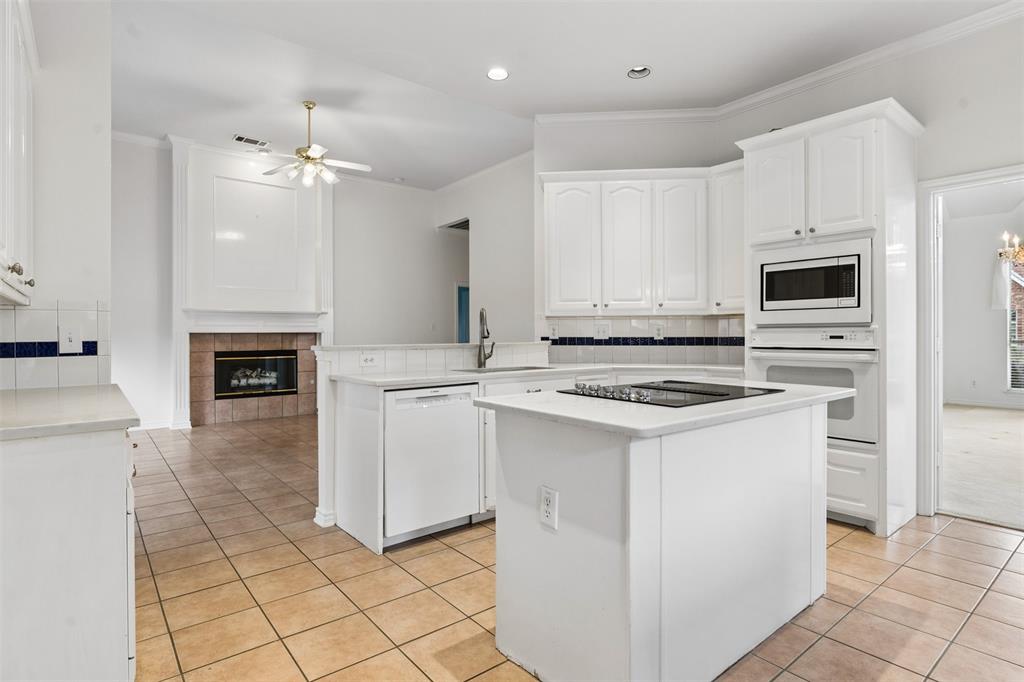 Kitchen featuring white cabinetry, center island with an integrated cooktop, built-in wall oven and microwave, ceramic tile flooring, and a fireplace with tile surround