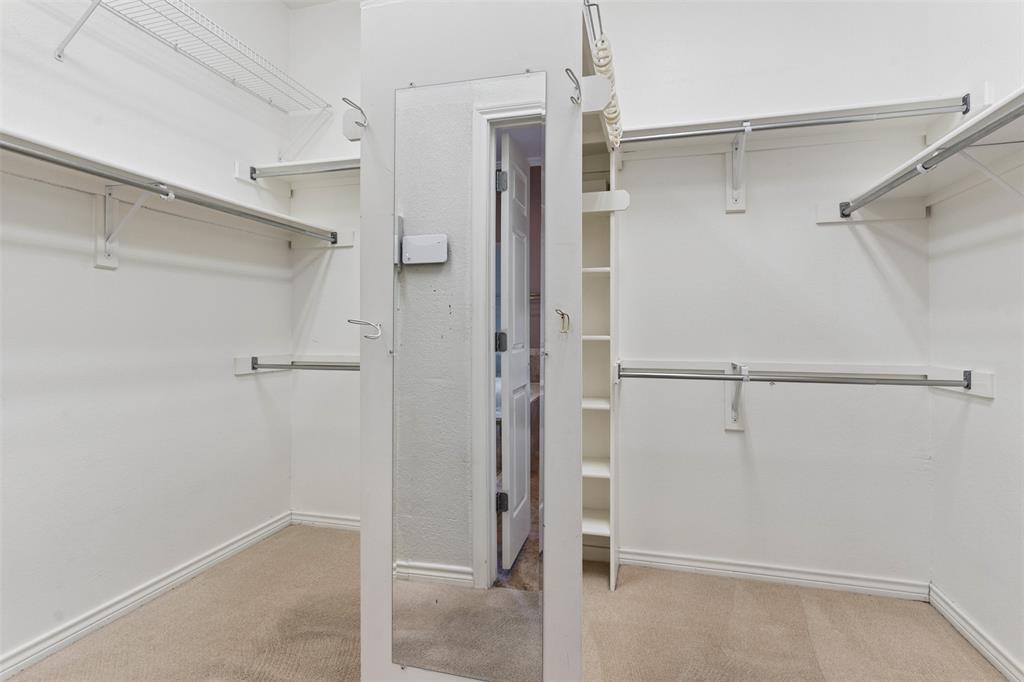 Walk-in closet featuring tiered metal garment rods, upper wire shelving, built-in vertical storage cabinetry, and a full-length wall-mounted mirror