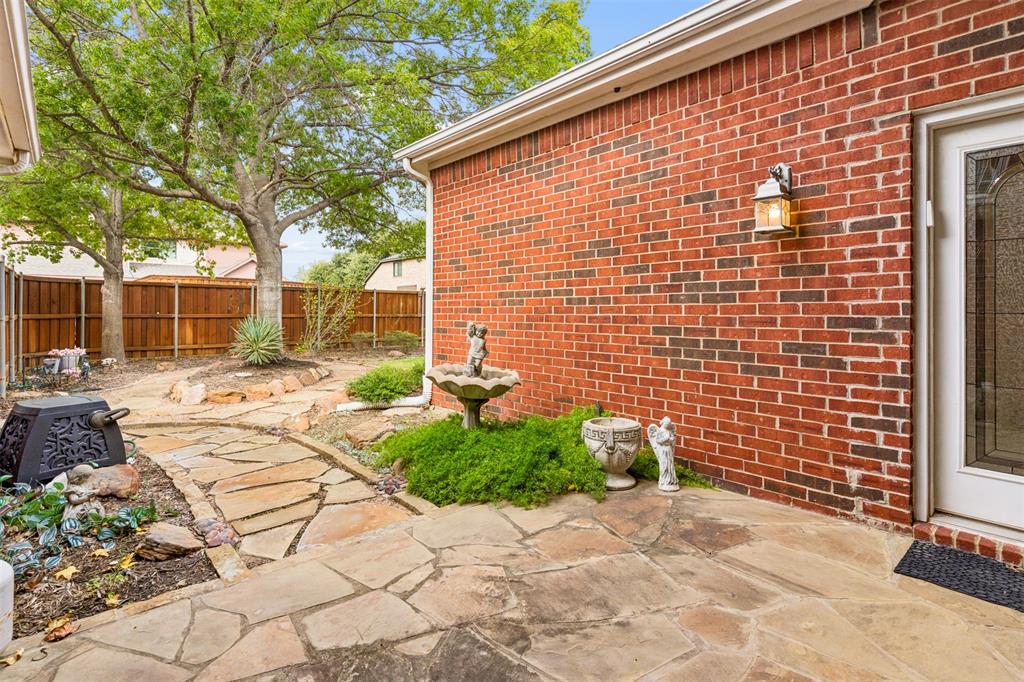 Exterior brick facade featuring a flagstone patio, winding natural stone pathway, and wood privacy fencing