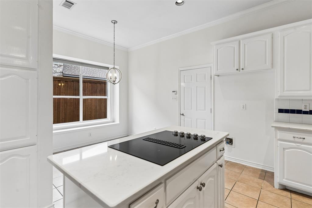 Kitchen island with a light-toned solid surface countertop and built-in electric cooktop, white cabinetry, tile flooring, and a multi-light pendant fixture