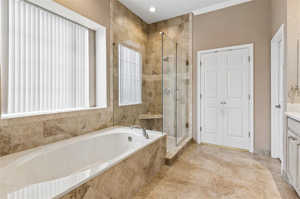 Oval soaking tub with stone tile surround, frameless glass-enclosed shower, neutral-tone wall finishes, and double-door entry