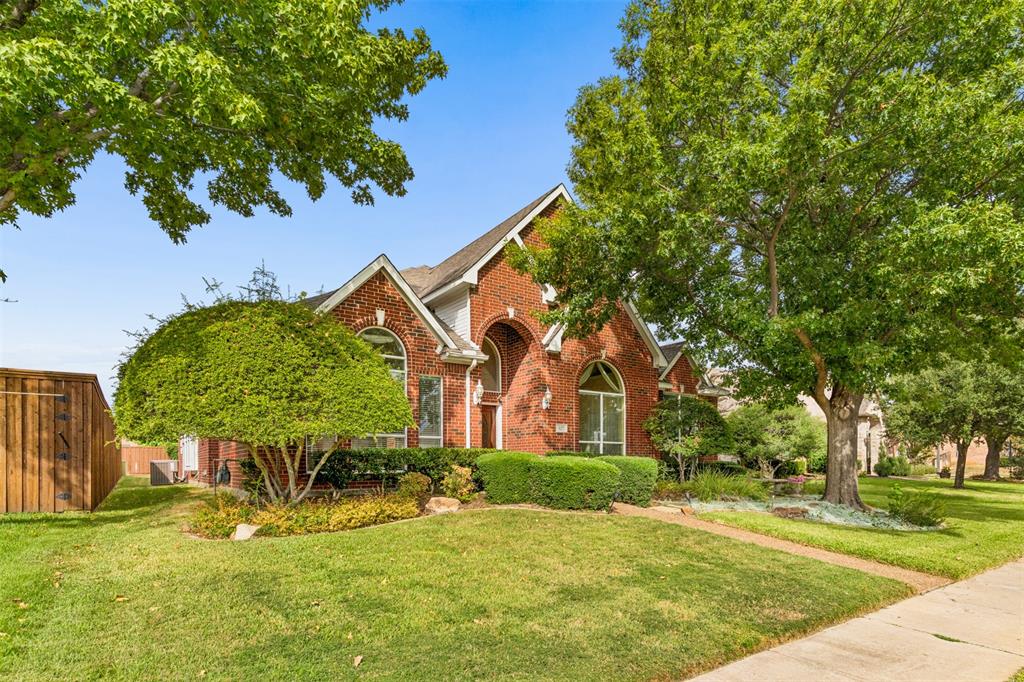 Brick exterior featuring an arched entryway, steep roof gables, and large arched windows, set on a landscaped lot with mature trees