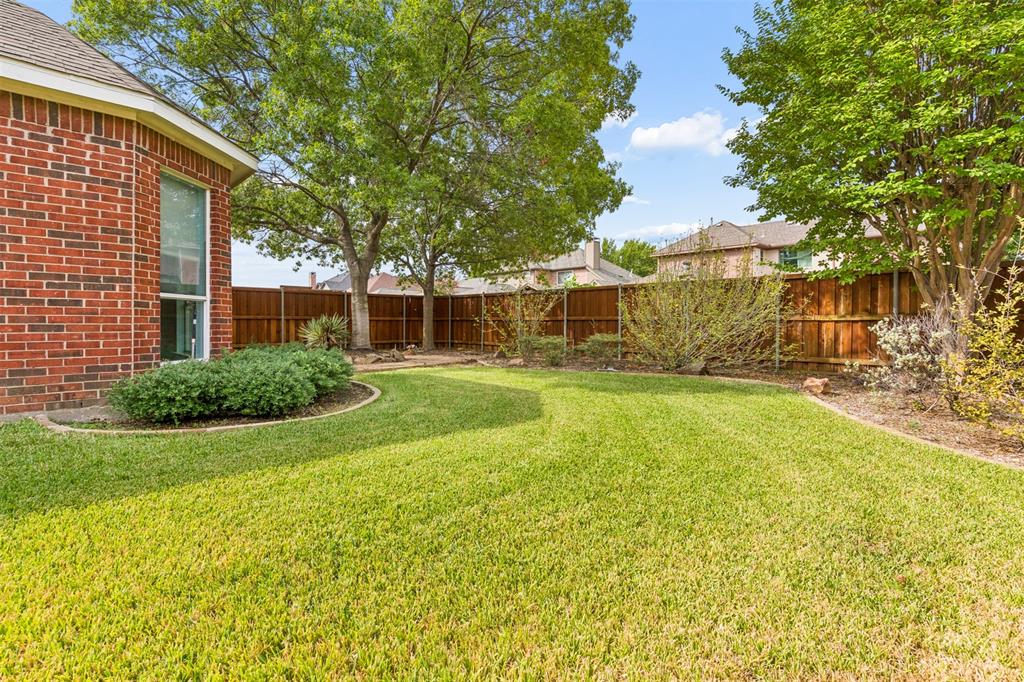 Backyard featuring a red brick exterior, manicured lawn, established shade trees, and a wooden perimeter fence