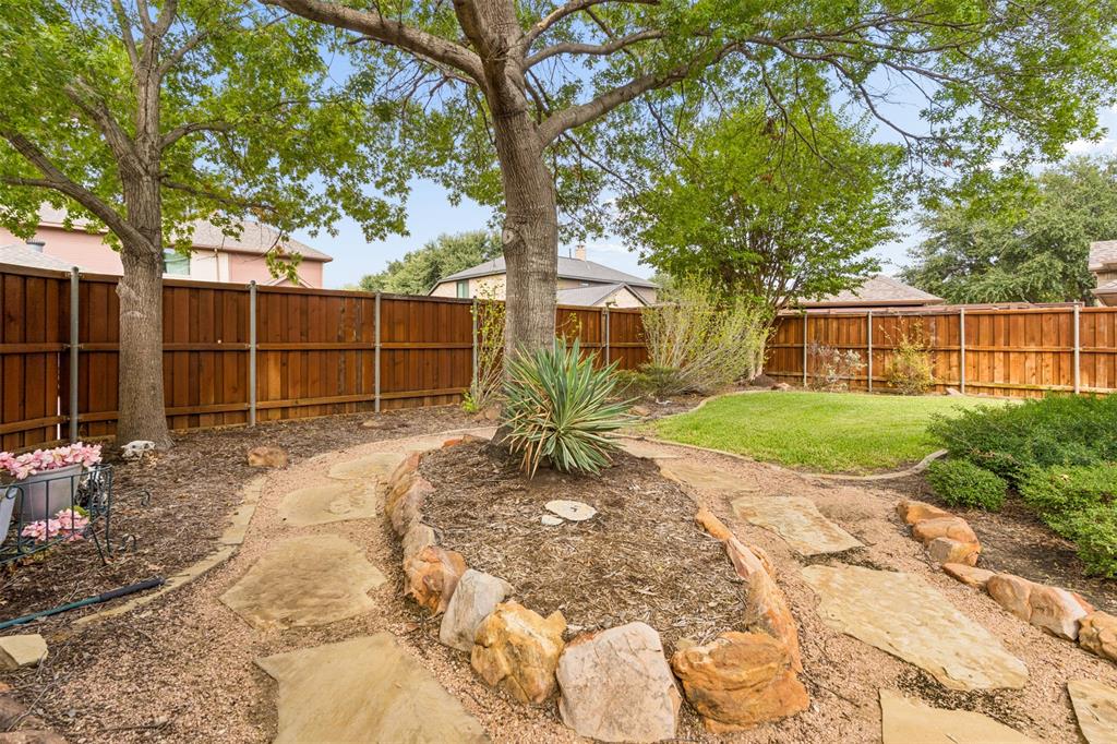 Backyard featuring a wood privacy fence, stone paver pathway, elevated stone-bordered garden bed, and mature trees