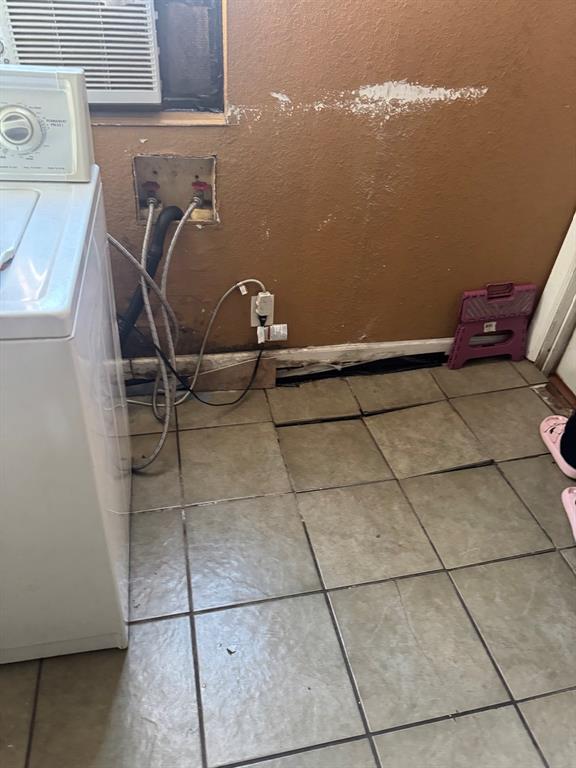 Laundry area featuring tile flooring, washer connections, and a window-mounted air conditioning unit.