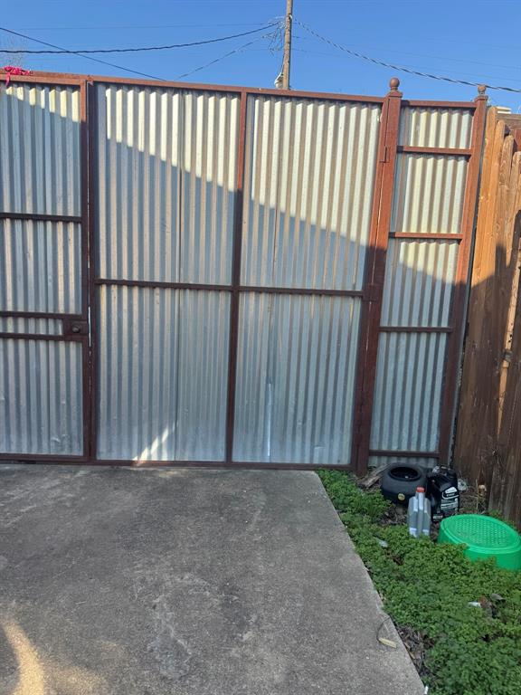Corrugated metal gate with a dark-toned frame and a concrete pad.