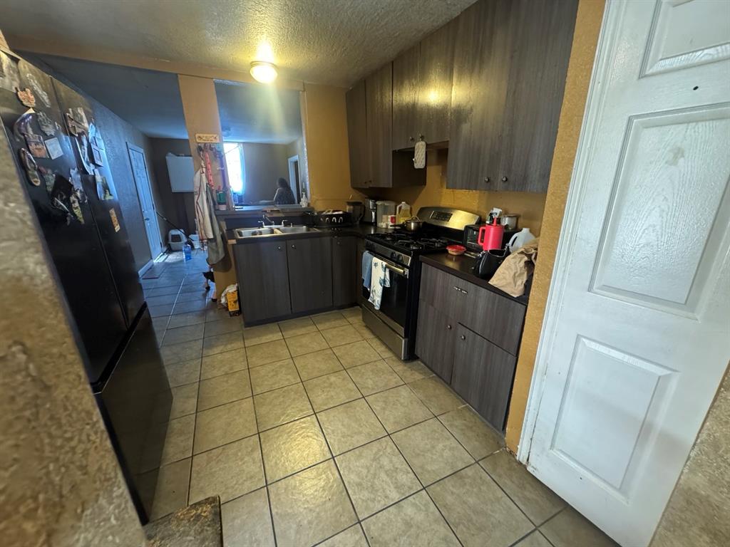 Kitchen featuring tile flooring, dark cabinetry, gas range, double-basin sink, and adjoining laundry area.