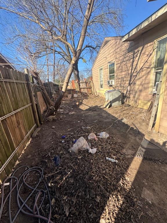 View of the side yard featuring mature trees, wood privacy fencing, and access along the exterior of the home.