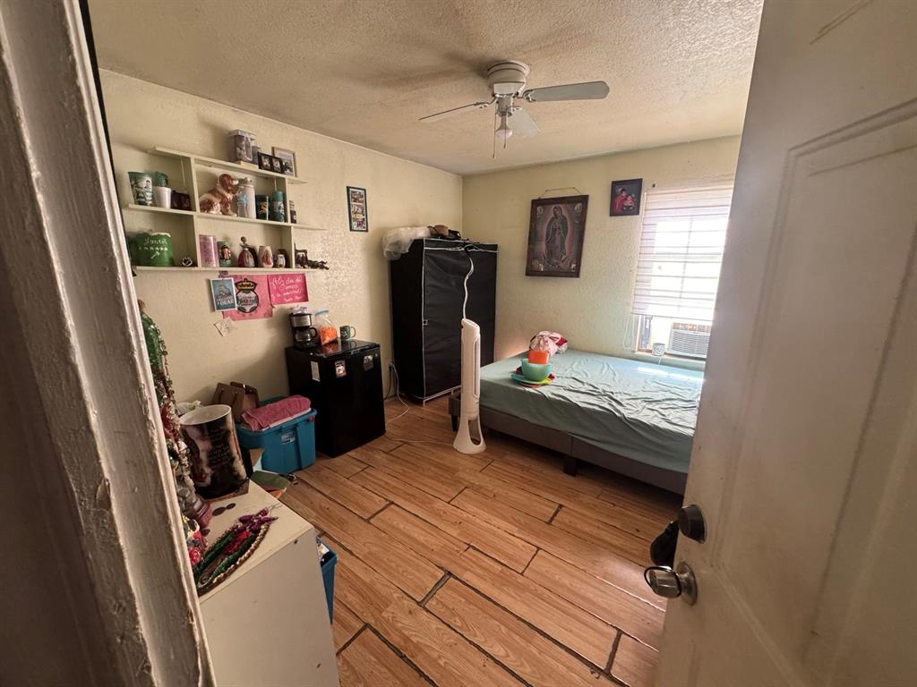 Bedroom featuring wood-look flooring, ceiling fan, wall-mounted shelving, and a window providing natural light.