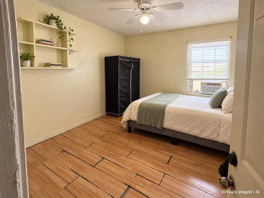 Bedroom featuring wood-look flooring, ceiling fan, and a window providing natural light. Virtually staged.