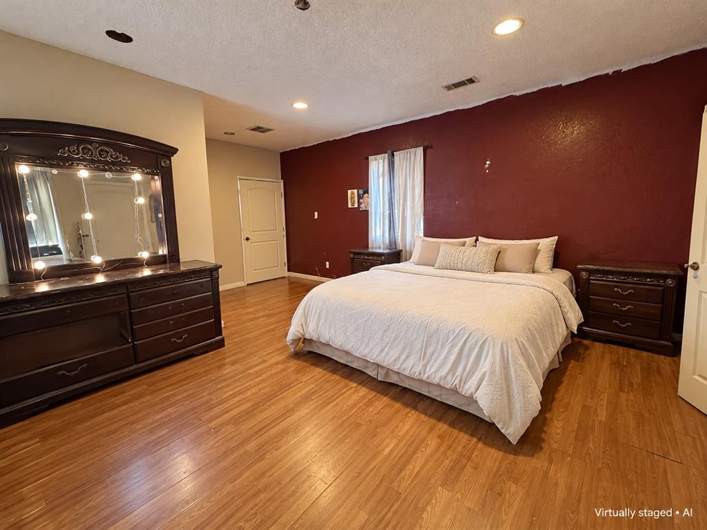 Spacious bedroom featuring wood-look flooring, recessed lighting, and a contrasting accent wall. Virtually staged for illustrative purposes.