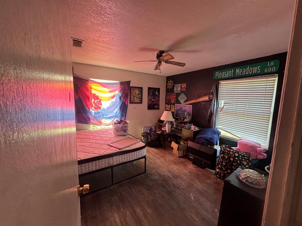 Bedroom featuring wood-look flooring, ceiling fan, contrasting accent wall, and two windows providing natural light.
