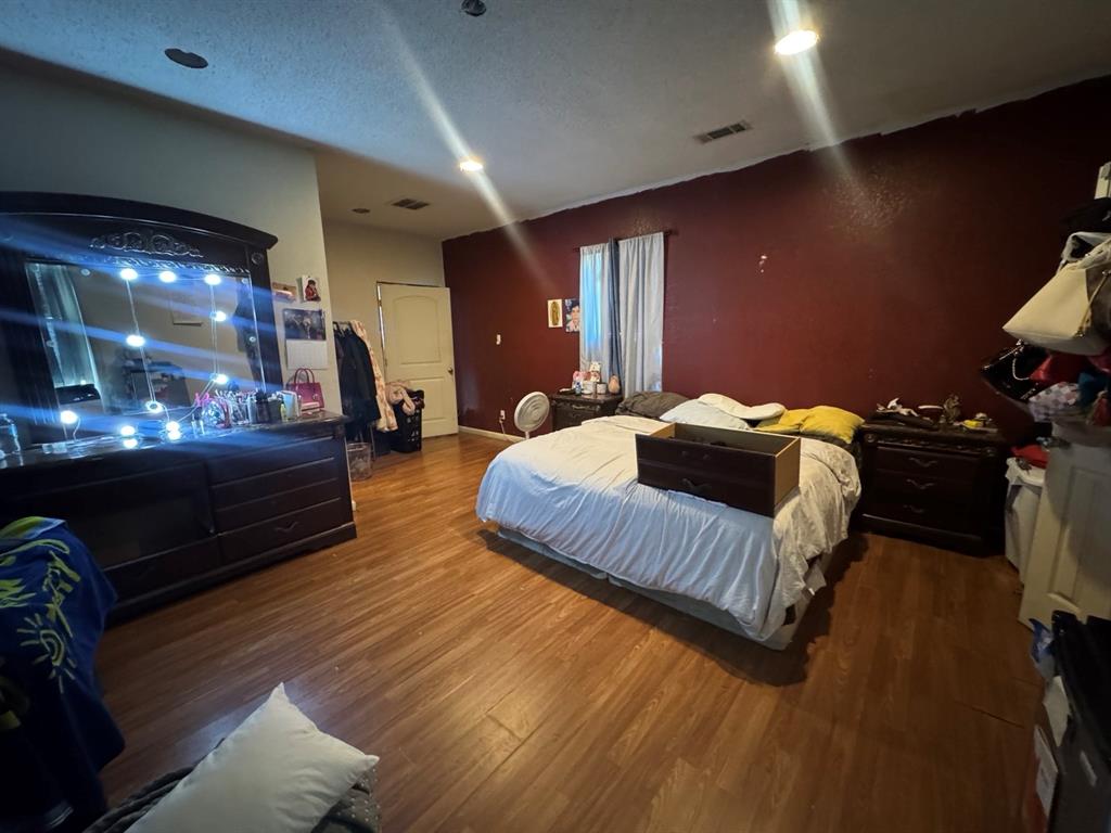 Spacious bedroom featuring wood-look flooring, recessed lighting, a contrasting accent wall, and room for additional furnishings.