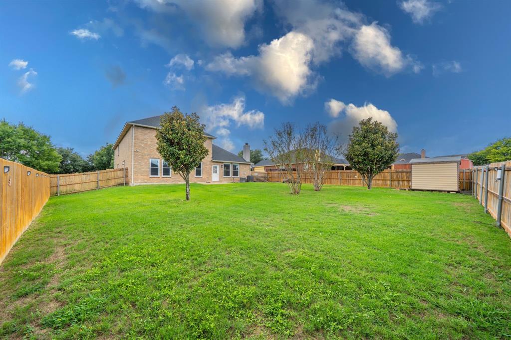 Backyard view of house, storage shed, wood privacy fence and large backyard.