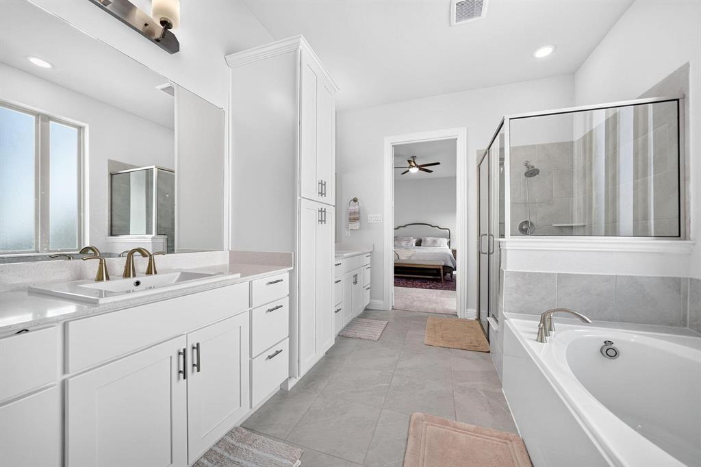 Bathroom featuring a white double vanity with stone countertops, a glass-enclosed shower, a deep soaking tub, and a tall linen storage cabinet