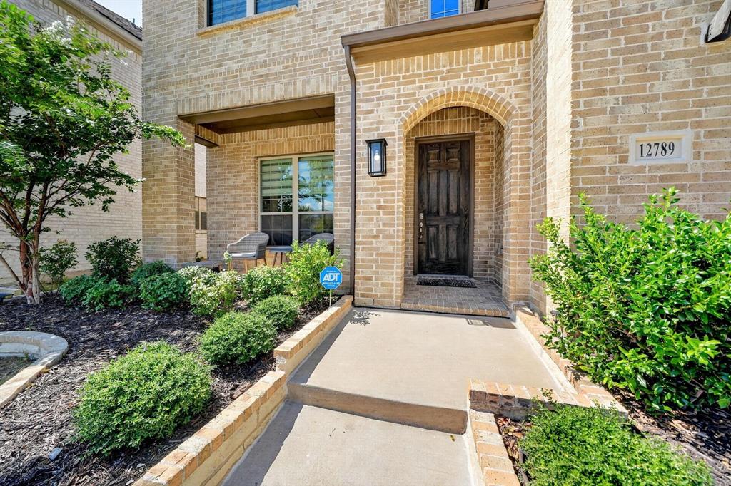 Brick exterior facade featuring a covered front porch, arched entryway, dark stained wood-finish front door, and manicured landscaping