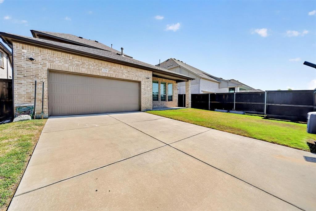 Brick exterior featuring a multi-car garage, concrete driveway, and a fenced lawn area