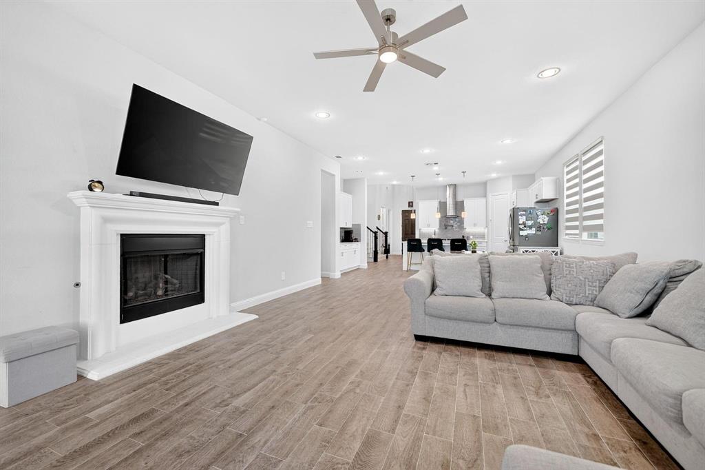 Open-concept interior featuring wood-finish tile flooring, recessed lighting, a ceiling fan, and a fireplace with a decorative mantel