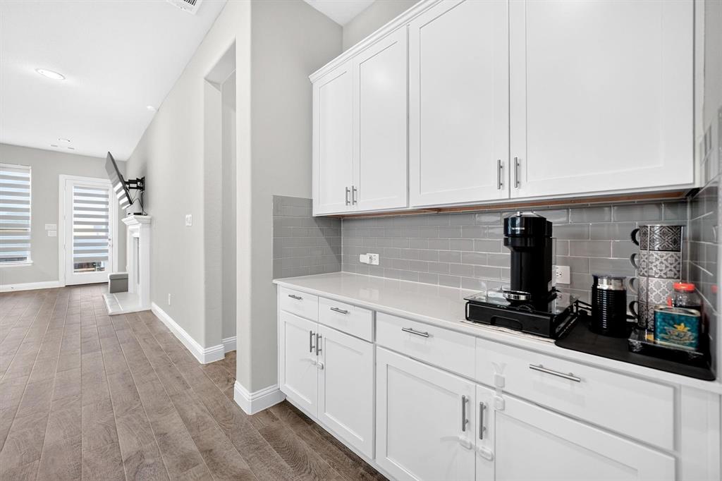 Built-in cabinetry featuring white shaker-style doors, stone-composite countertops, and a gray subway tile backsplash, complemented by wood-finish flooring and a recessed fireplace