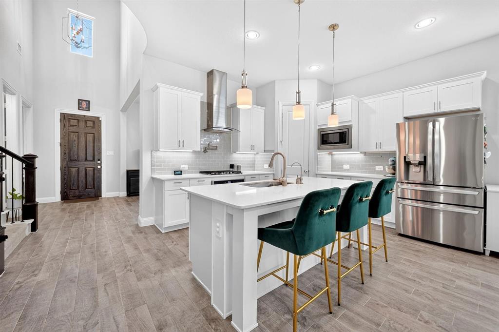 Kitchen featuring white cabinetry, an expansive central island with quartz countertops, wood-finish flooring, stainless steel appliances, and high ceilings