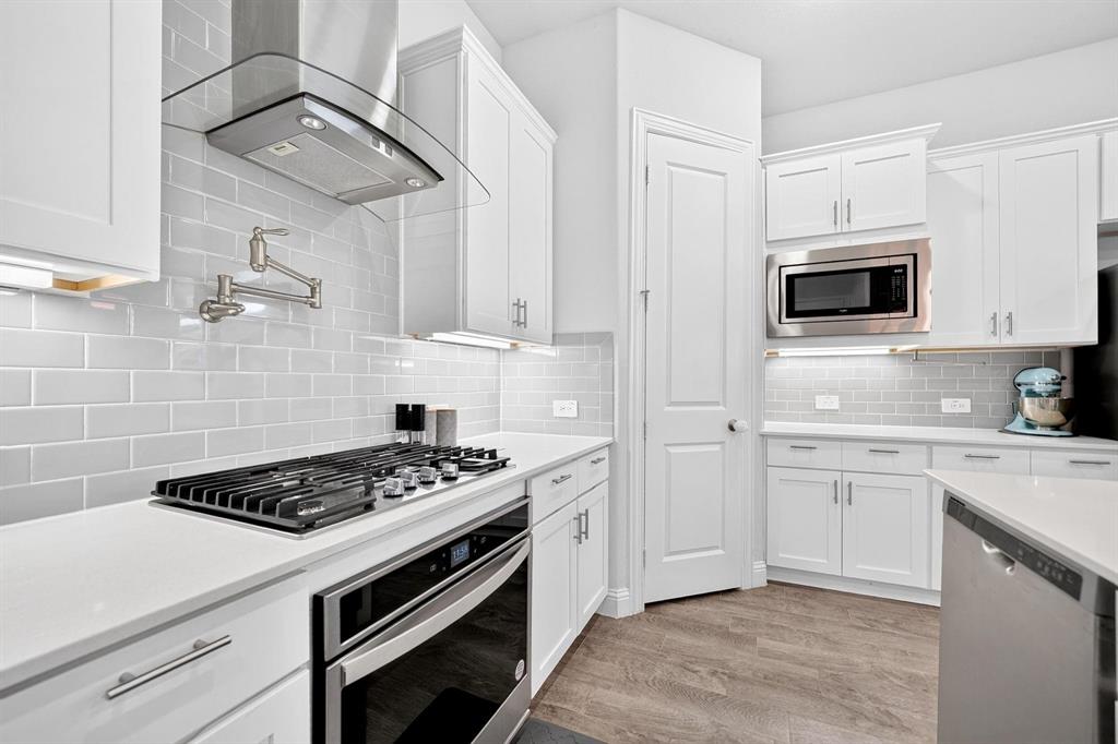 Kitchen featuring white shaker-style cabinetry, quartz countertops, subway tile backsplash, stainless steel gas cooktop with wall-mounted pot filler, and wood-finish flooring