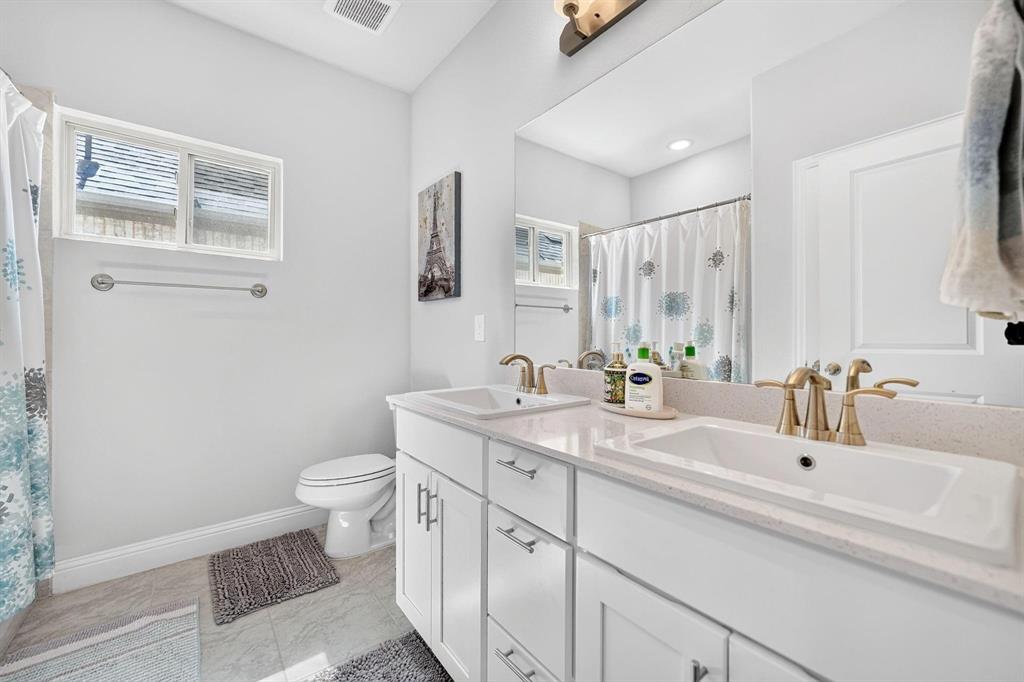 Dual-sink vanity with white cabinetry, light-toned stone-finish countertop, undermount sinks, and metallic finish faucets featuring a large wall-mounted mirror