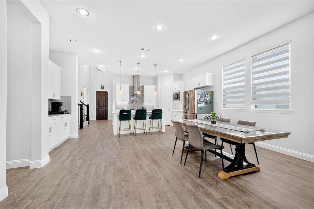 Open-concept kitchen and dining area featuring wood-finish flooring, recessed lighting, white cabinetry, a kitchen island with pendant lighting, and horizontal banded window treatments
