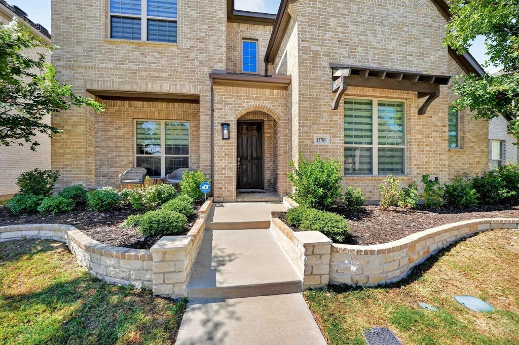 Brick exterior with a stone-accented arched entryway, tiered stone retaining walls, and a wood-bracketed window awning