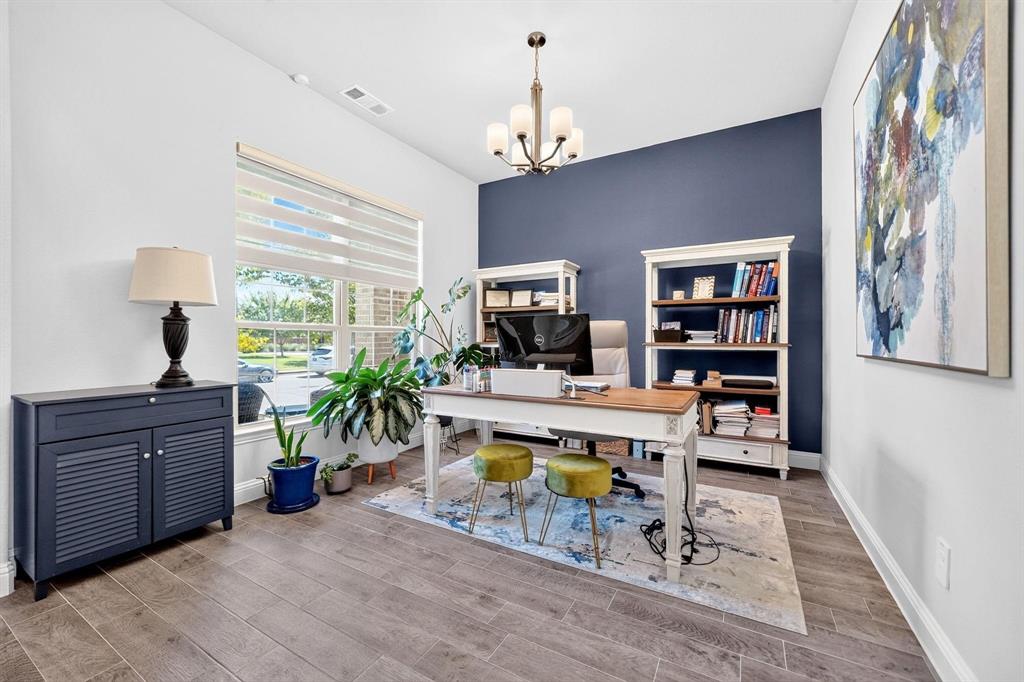 Room featuring wood-finish tile flooring, a deep-toned accent wall, large window with integrated blinds, and a multi-arm chandelier