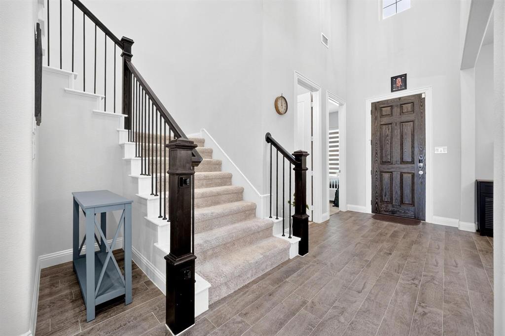 Foyer featuring high ceilings, wood-finish flooring, a dark-stained six-panel entry door, and a staircase with carpeted treads and dark-stained newel posts