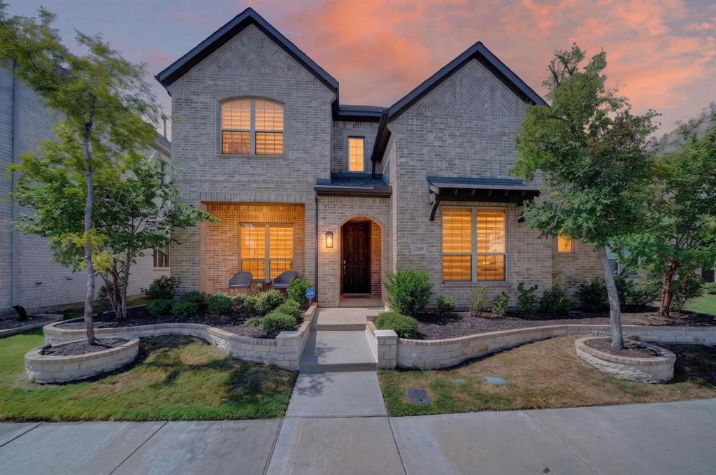 Two-story brick exterior featuring a multi-gabled roofline, decorative herringbone masonry details, arched entryway, and stone-retained landscaping