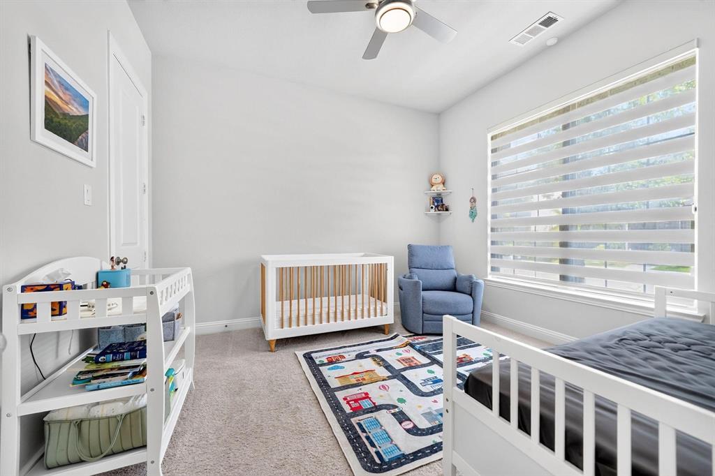 Neutral-toned interior featuring plush carpeting, a multi-blade ceiling fan with integrated lighting, and a large window fitted with horizontal light-filtering shades