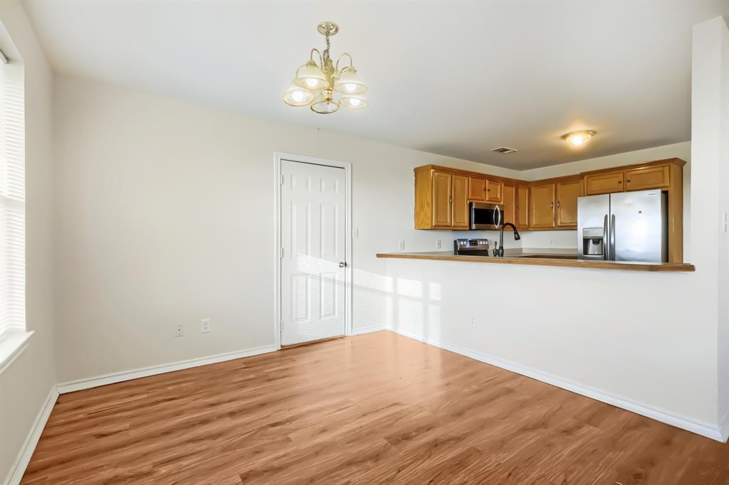 Dining and eat at bar featuring laminate wood-finish flooring, wood cabinetry, stainless steel kitchen appliances, kitchen pass-through counter, and multi-light chandelier