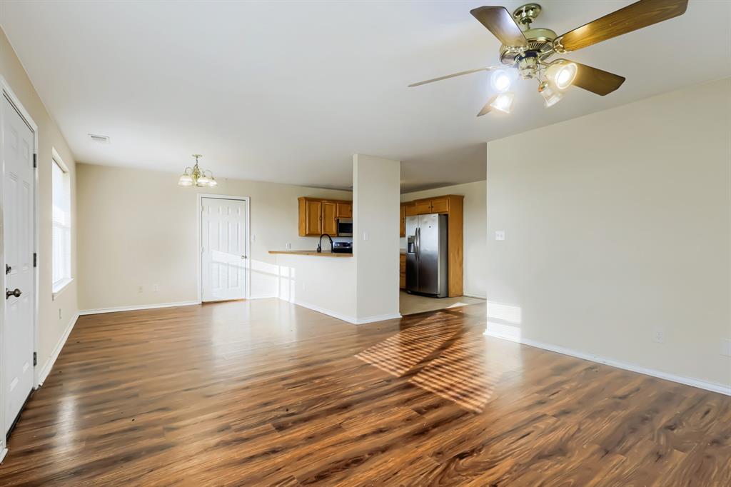 Open-concept interior featuring laminate wood-finish flooring, a ceiling fan with integrated lighting, kitchen cabinetry, and stainless steel appliances