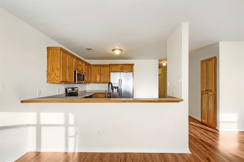 Kitchen featuring wood cabinetry, stainless steel appliances, breakfast bar, and laminate wood-finish flooring throughout living spaces.