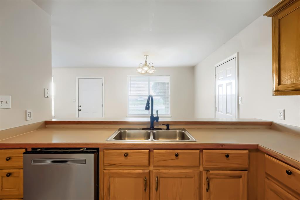 Kitchen featuring wood cabinetry, stainless steel dishwasher space, dual-basin sink, matte black gooseneck faucet, and solid-surface countertop