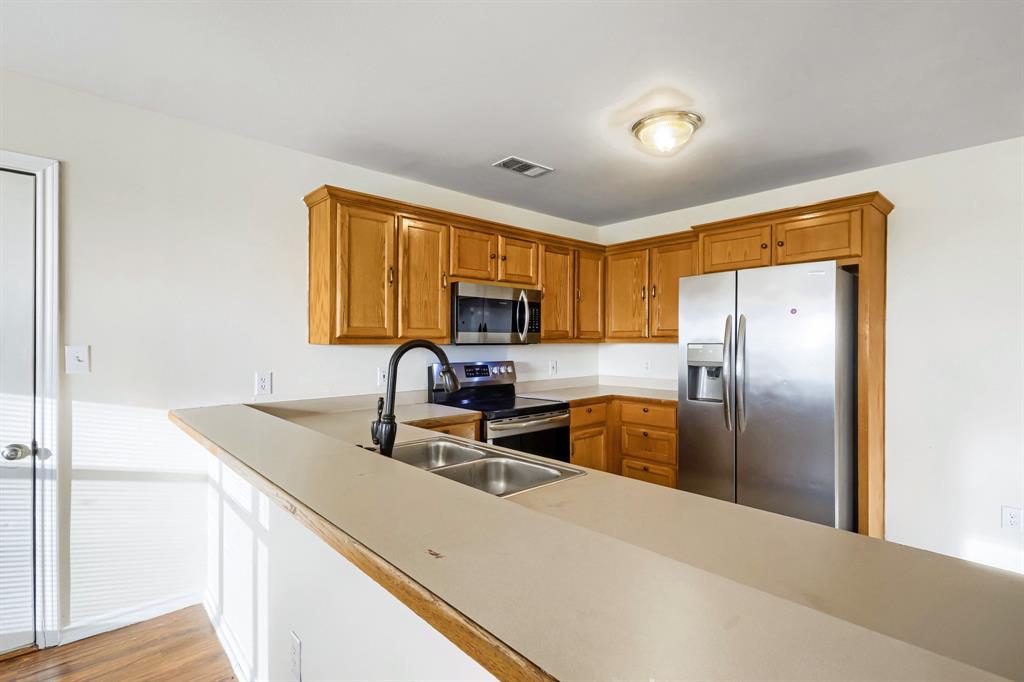 Kitchen featuring natural wood cabinetry, solid surface countertops, a stainless steel side-by-side refrigerator, built-in microwave, and a double-basin sink with a high-arch matte black faucet
