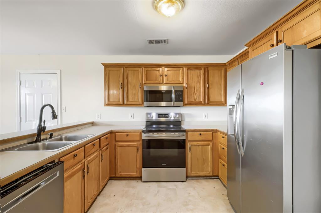 Kitchen featuring wood cabinetry, stainless steel appliances, dual-basin sink with matte black faucet, and solid-surface countertops