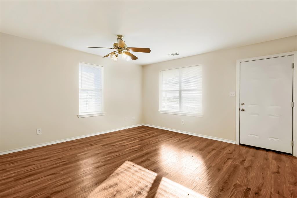 Interior space featuring laminate wood-finish flooring, neutral wall paint, two windows, and a ceiling fan with integrated lighting