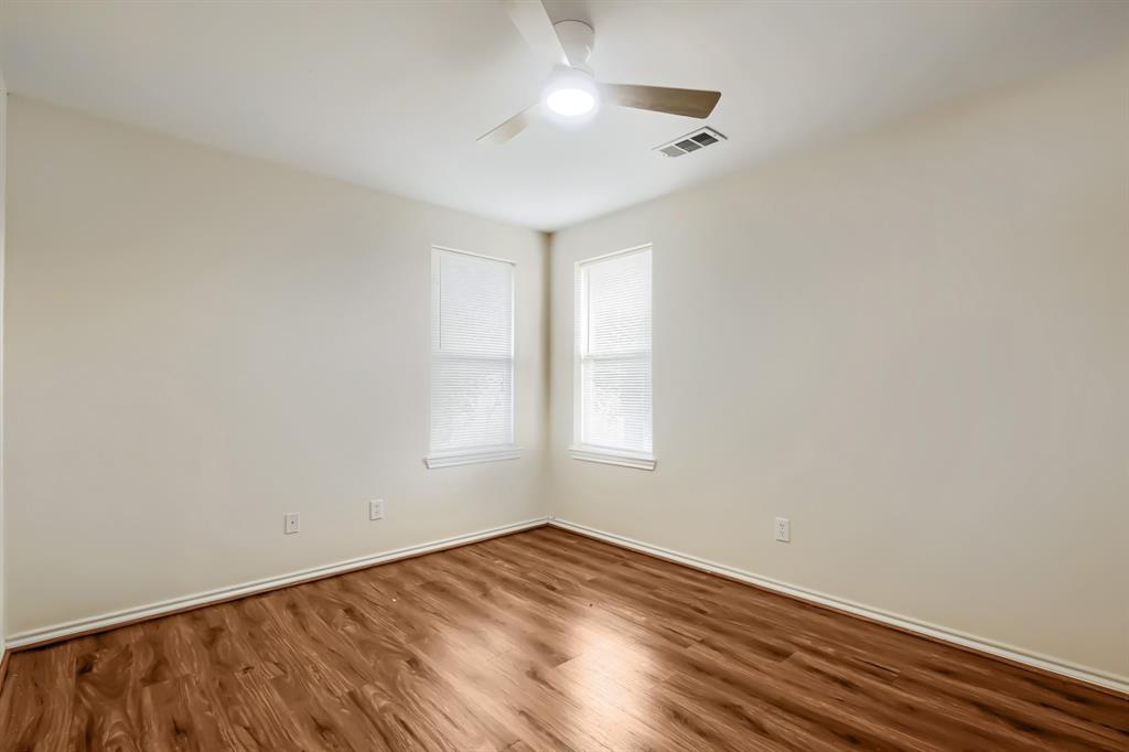 Neutral wall tones, wood-finish flooring, two windows with blinds, and a ceiling fan with integrated lighting