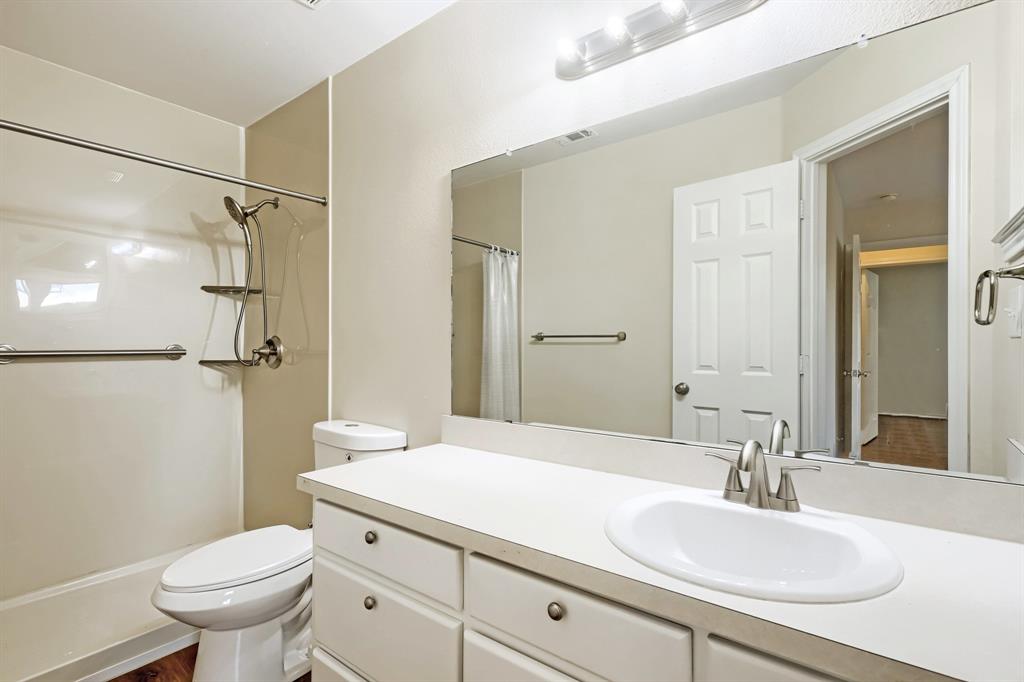 Bathroom featuring a white vanity with a countertop basin, large wall-mounted mirror, brushed metal hardware, and a tub-shower combination with an integrated shelving unit and grab bar