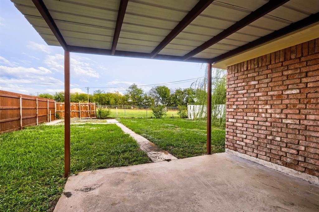 Covered concrete patio with metal roof framing, red brick exterior wall, and wood-panel privacy fencing enclosing a lawn area