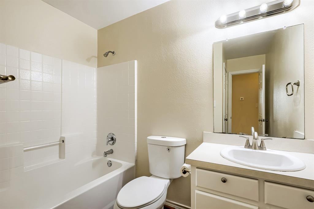 Bathroom featuring a vanity with an integrated basin, a white-tiled tub and shower enclosure, a rectangular wall-mounted mirror, and a multi-bulb vanity light fixture