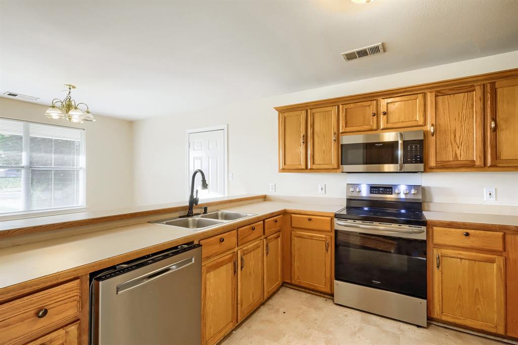 Kitchen featuring wood cabinetry, stainless steel appliances, a dual-basin sink with a matte black faucet, and solid-surface countertops Kitchen featuring wood cabinetry, stainless steel appliances, a dual-basin sink with a matte black faucet, and solid-surface countertops