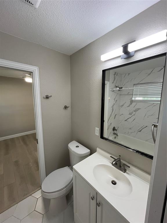 Bathroom featuring a white vanity cabinet with a integrated sink, framed mirror, modern linear wall-mounted lighting, tub enclosure with decorative tile surround, and hexagonal tile flooring