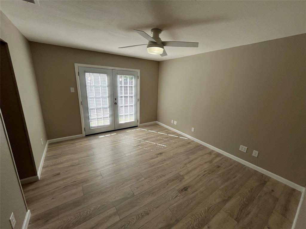 Room featuring wood-finish flooring, white French doors, and a ceiling fan with integrated lighting