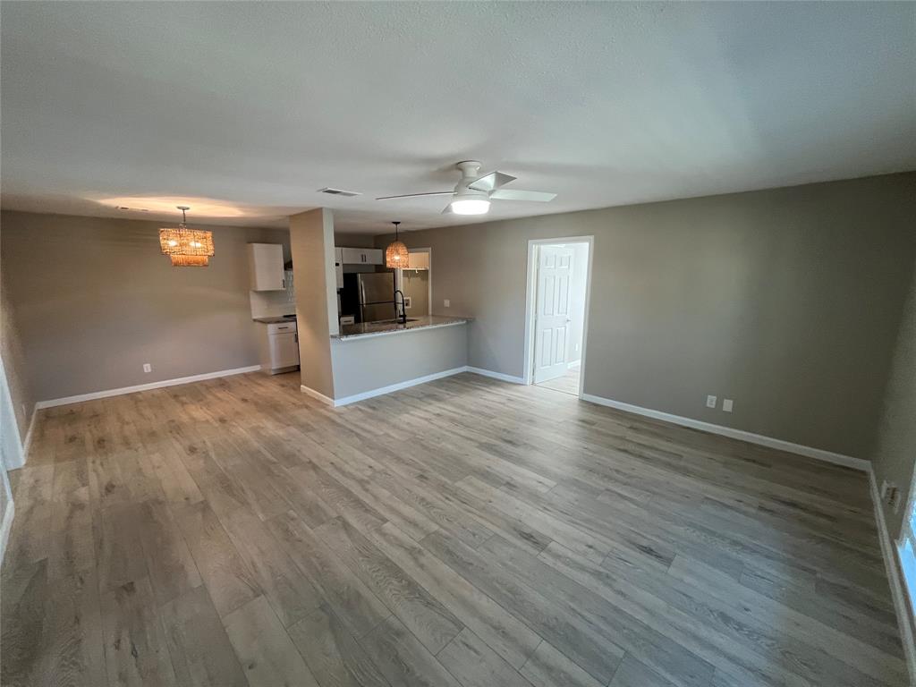 Open-concept space featuring wood-finish flooring, a kitchen peninsula with stone-surface countertop, modern pendant lighting, and a ceiling fan