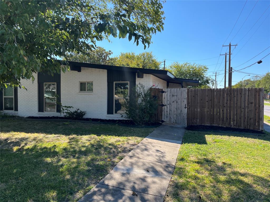 Mid-century modern exterior featuring painted brick facade, flat roofline with exposed rafter tails, vertical trim accents, and a wood privacy fence Mid-century modern exterior featuring painted brick facade, flat roofline with exposed rafter tails, vertical trim accents, and a wood privacy fence