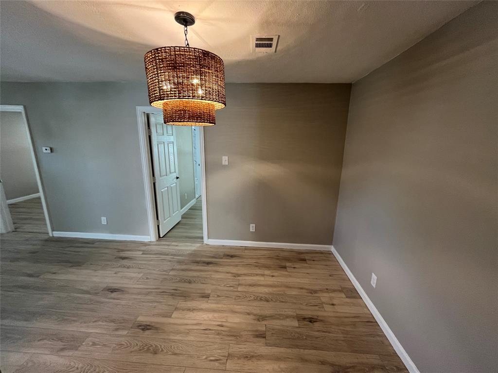 Room featuring wood-finish flooring, neutral wall paint, and a tiered woven-texture drum pendant light