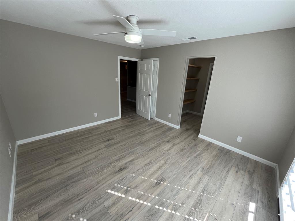 Room featuring wood-finish flooring, a white ceiling fan with integrated lighting, and a walk-in closet with built-in shelving